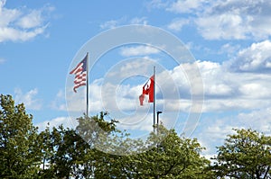 United states and Canadian flags against blue sky with clouds