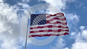 United States flag flying in breeze, blue sky and cloudy background, slow motion