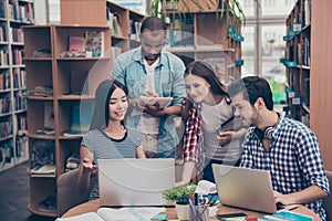 Unity and connection of people. Four multi ethnic students friends, doing research in library together, wearing casual clothes, e