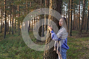 Unity with nature: young calm girl hugging pine tree trunk with closed eyes walking in autumn forest