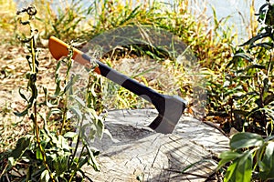 Universal orange red black modern axe with Shock absorbing fibreglass handle on dry stump log on lake coast in grass. Hiking and