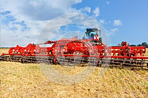 Universal red harrow as a hitch on an agricultural tractor against the background of a compressed yellow wheat field