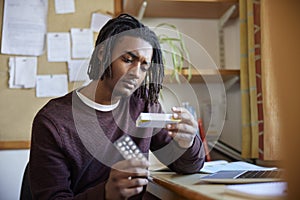 University Or College Student With Poor Mental Health Looking At Anti Depressant Medication Packaging At Desk In Room