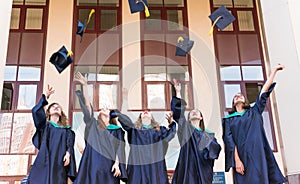 University graduates  throwing graduation hats in the air. Group of happy graduates in academic dresses near university building