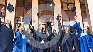 University graduates  throwing graduation hats in the air. Group of happy graduates in academic dresses near university building