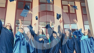 University graduates  throwing graduation hats in the air. Group of happy graduates in academic dresses near university building