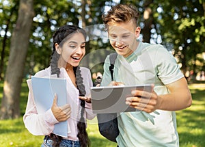 University lifestyle concept. Student guy showing digital tablet to girlfriend, looking at test results outdoors