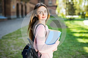 University student girl looking happy smiling with book or notebook in campus park.