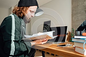 University student leaf through a book while going online lesson