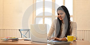 A university student is learning lessons online while sitting at the wooden working desk