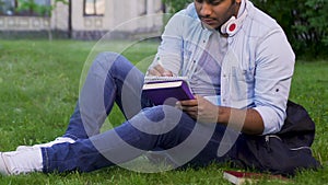 University student sitting on grass, writing essay, literary studies project