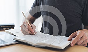 University student using laptop or computer for studying or learning book, reading textbook at home. Knowledge and skill training