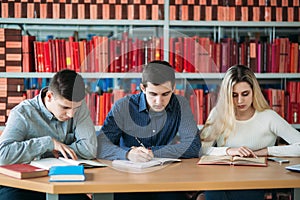 University students sitting together at table with books and laptop. Happy young people doing group study in library