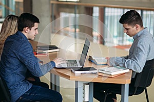 University students sitting together at table with books and laptop. Happy young people doing group study in library