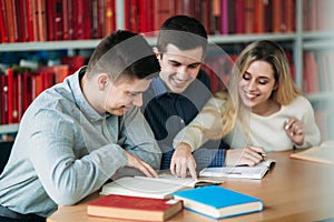 University students sitting together at the table with books and laptop. Happy young people doing group study in library