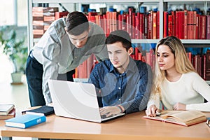 University students sitting together at table with books and laptop. Happy young people doing group study in library