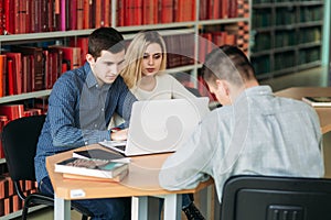 University students sitting together at table with books and laptop. Happy young people doing group study in library