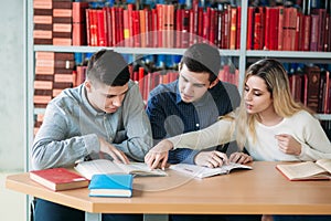 University students sitting together at table with books and laptop. Happy young people doing group study in library