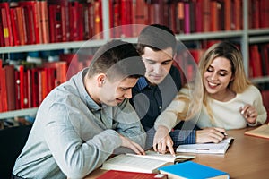 University students sitting together at table with books and laptop. Happy young people doing group study in library