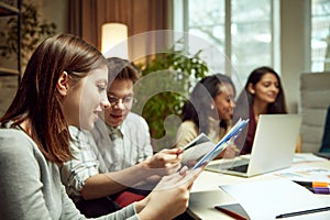 University students sitting together at table with books and laptops, studying together, doing projects