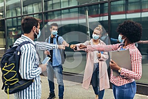 Students standing and greeting with a fist outdoors, coronavirus and back to normal concept