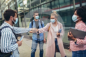 Students standing and greeting with a fist outdoors, coronavirus and back to normal concept