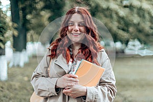 University young caucasian female student wearing glasses with books outside campus. Fiery curly hair