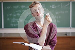 University young male professor teaching students in university holding notebook with chalk