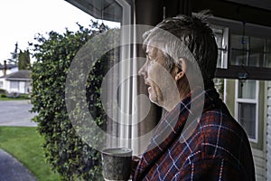 Unkept older man with bed head in housecoat looking out window