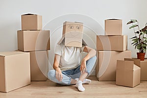 Unknown anonymous woman wearing white t shirt sitting on floor surrounded with cardboard boxes with belongings, having carton box