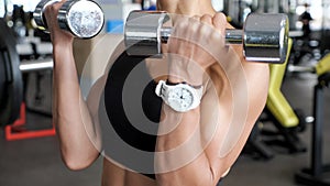 Unknown athletic woman is making set of reps exercise for biceps with dumbbells in hands in gym