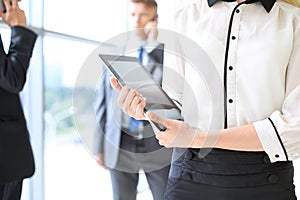 Unknown business woman using tablet computer in office hall among businesspeople