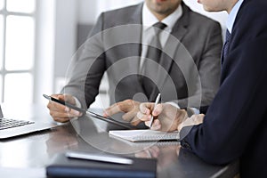 Unknown businessman using tablet computer and working together with his colleague while sits at the glass desk in modern