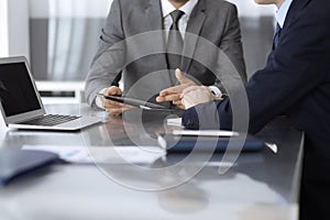 Unknown businessman using tablet computer and working together with his colleague while sits at the glass desk in modern