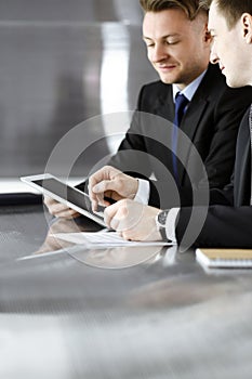 Unknown businessmen using tablet computer and work together at the glass desk in modern office, close-up. Teamwork and
