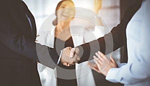 Unknown businesspeople are shaking their hands after signing a contract, while standing together in a sunny modern