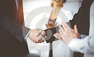 Unknown businesspeople are shaking their hands after signing a contract, while standing together in a sunny modern