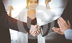 Unknown businesspeople are shaking their hands after signing a contract, while standing together in a sunny modern