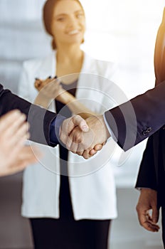 Unknown businesspeople are shaking their hands after signing a contract, while standing together in a sunny modern