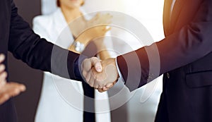 Unknown businesspeople are shaking their hands after signing a contract, while standing together in a sunny modern