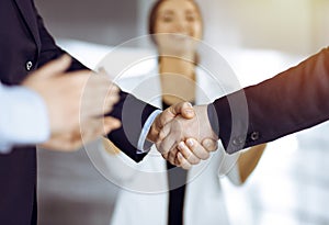 Unknown businesspeople are shaking their hands after signing a contract, while standing together in a sunny modern