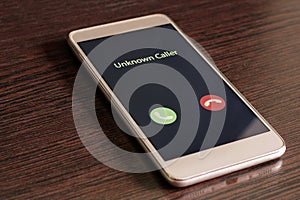 Unknown caller. White smartphone with incoming call from an unknown number on a wood table background. Incognito or anonymous