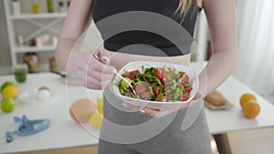 Unknown Caucasian girl mixing vegetables and oil in bowl at home. Unrecognizable slender woman preparing fresh spring