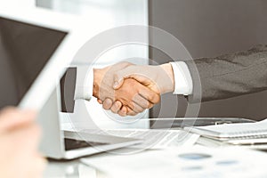 Unknown diverse business people are shaking hands finishing up meeting at the desk in office, close-up. Handshake