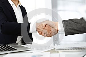 Unknown diverse business people are shaking hands finishing up meeting at the desk in office, close-up. Handshake