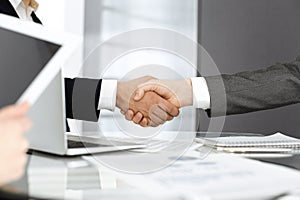 Unknown diverse business people are shaking hands finishing up meeting at the desk in office, close-up. Handshake