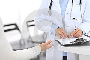 Unknown doctor and female patient discussing something while standing near reception desk in emergency hospit