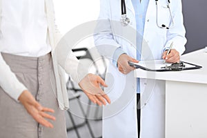 Unknown doctor and female patient discussing something while standing near reception desk in emergency hospit