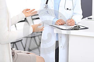 Unknown doctor and female patient discussing something while standing near reception desk in emergency hospit