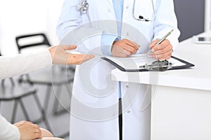 Unknown doctor and female patient discussing something while standing near reception desk in emergency hospit